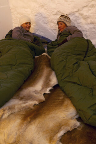 Two women in sleeping bags on reindeer hides in an igloo hotel room at Sorrisniva, Alta by Sorrisniva